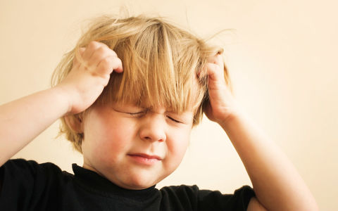 En liten gutt med halvlangt hår lukker øynene imens han klør seg i hodebunnen med begge hender.