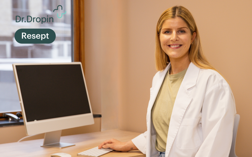 Kvinnelig lege fra Dr.Dropin sitter smilende ved PC