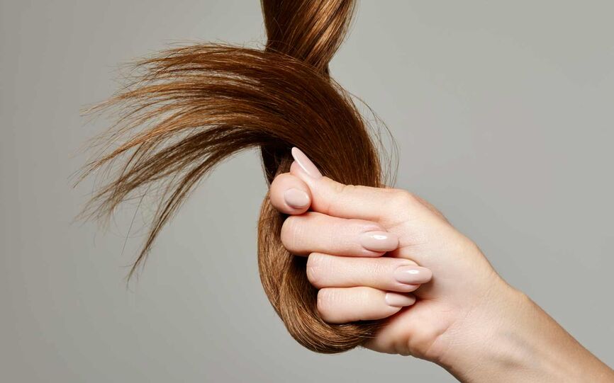 Bilde av en hånd som holder en fast en del av langt hår neven. Håret tvunnet rundt i en knute og ser sterkt og glansfullt ut.